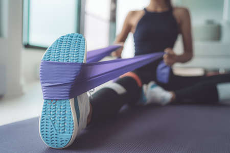 Resistance band exercise at home. Woman doing pilates workout using elastic strap pulling with arms...