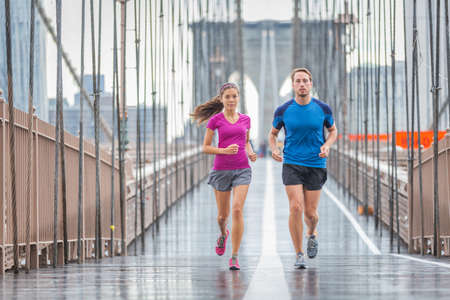 New York city runners athletes training for run marathon on Brooklyn Bridge. Fit active interracial couple on outdoor running exercise in raining day. Summer rain. Asian woman, Caucasian manの写真素材