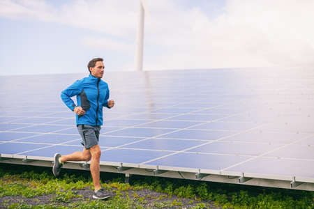 Active lifestyle young runner man running by solar panels farm outdoors summer background