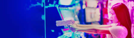 Asian woman playing vintage arcade shooting game at japanese gaming cyber arcade cafe. Action video machine girl having fun to shoot targets on screen of videogame simulator banner.の写真素材