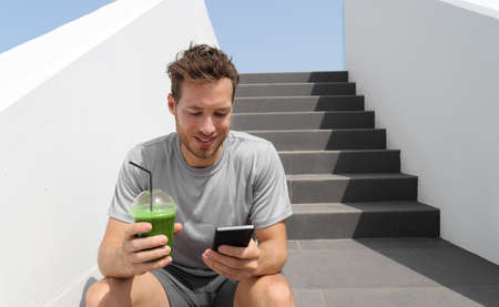 Green smoothie juice drink man drinking detox diet protein shake using mobile phone app for tracking...