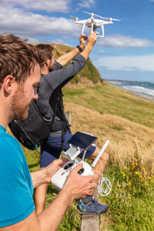 Friends flying drone together - group of two guys having fun playing with drone outdoors at take-offの写真素材