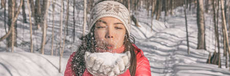 Winter Asian young woman blowing on snow for fun playing outdoor in nature forest. happy girl banner panoramic wearing cold weather accessoriesの写真素材