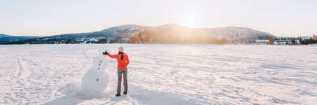 Winter fun activity. Girl making snowman in winter lake snow nature landscape. Panoramic bannerの写真素材