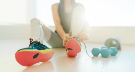 Fitness at home getting in shape for New Year resolution. Woman lacing running shoes for indoor workout cardio floor exercise on yoga mat. Banner panoramic active lifestyleの写真素材