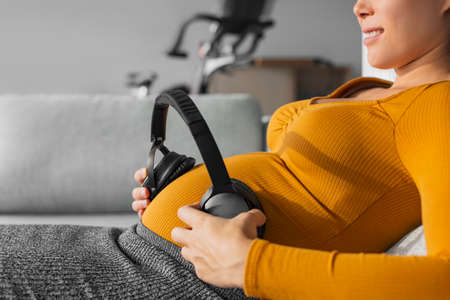 Pregnancy music. Pregnant woman holding headphones to foetus in womb against belly to hear soundsの写真素材