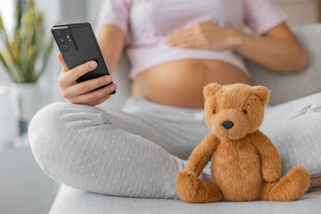 Pregnancy app for maternity prenatal online class. Pregnant woman using mobile phone with focus on...