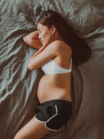 Sleeping pregnant woman top view of pregnancy belly during first trimester. Asian girl in pajamas...
