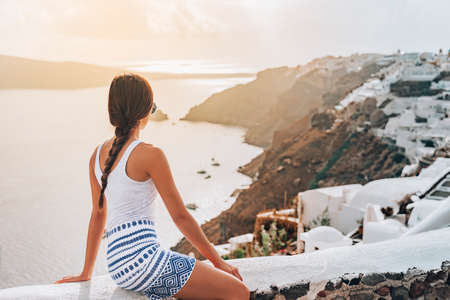 Greece luxury travel travel tourist woman watching sunset from Santorini island relaxing at Mediterranean sea view from coast of greek island. Europe Greece destination elegant young lady beautyの写真素材