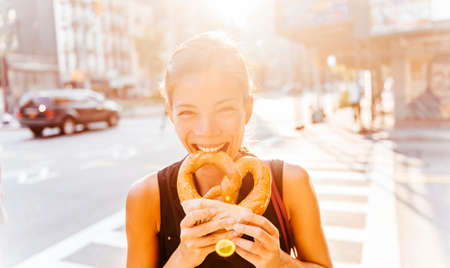 Woman eating pretzel in Manhattan, a classic New York City snack. Multiracial asian young...