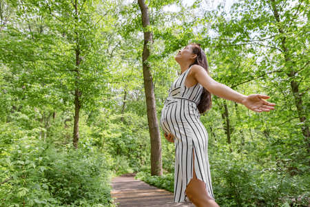 Pregnant woman happy in sustainable forest nature outdoors with open arms in freedom. Health, eco-friendly environment conservation concept. Pregnancy lifestyleの写真素材