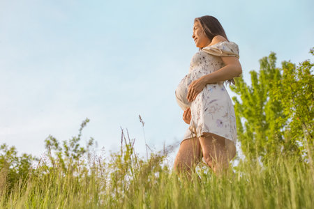 Pregnant woman in 3rd trimester breathing clean air during pregnancy in fresh spring forest nature. Asian girl holding expecting tummy in happiness and healthy and wellnessの写真素材
