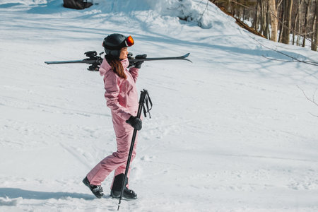 Winter Skiing. Ski portrait of woman alpine skier holdings skis wearing helmet, cool ski goggles, hardshell winter jacket and ski gloves on snow covered ski trail slopeの写真素材