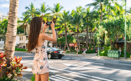 Honolulu city woman tourist taking pictures with phone camera walking on street in Waikiki, Oahu, Hawaii. USA summer travelの写真素材