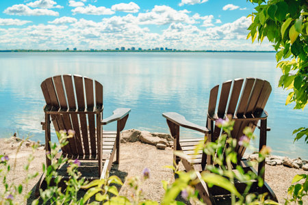 Two Muskoka chairs by the water on home terrace with calm view of lake in Canada. Summer cottage vacation lifestyleの写真素材