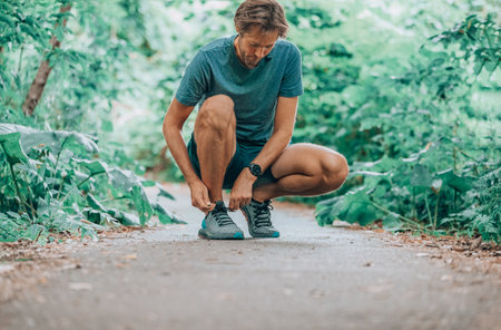 Running shoes sports smartwatch man tying shoe laces. Male fitness runner getting ready to jog in...