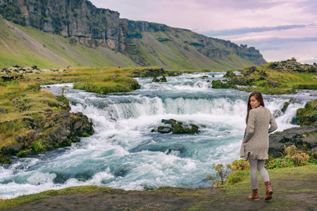 Iceland. Woman by waterfall on Iceland. Multiracial woman portrait in casual clothing visiting icelandic nature landscapeの写真素材
