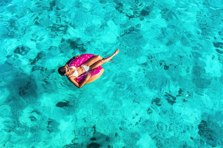 Beach vacation woman relaxing in pool float donut inflatable ring floating on turquoise ocean water background in Caribbean travel summer. Girl in white bikini top drone view.の写真素材