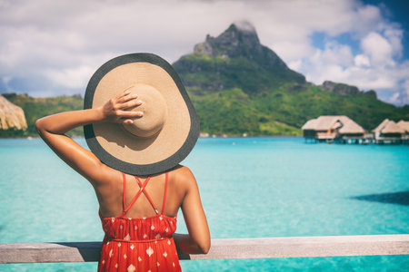 Beach vacation travel getaway summer holiday woman looking at view of Mt Otemanu on Bora Bora luxury hotel on romantic honeymoon. Tourist holding hat from behind enjoying Tahiti, French Polynesia.の写真素材