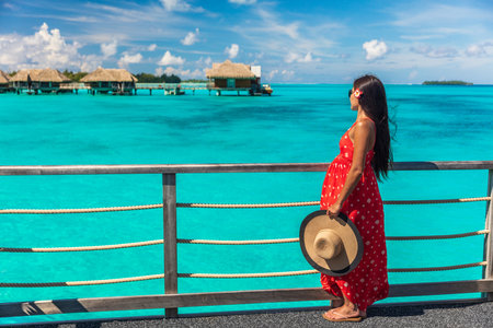 Pregnant woman tourist on summer vacation. Pregnancy on travel holiday luxury paradise resort hotel girl wearing sun hat and dress walking in Bora Bora, Tahiti, French Polynesia.の写真素材