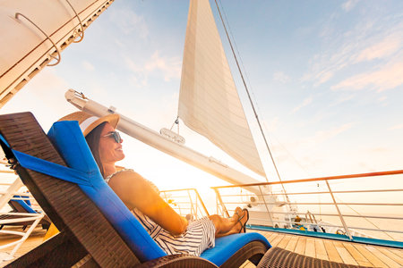 Luxury cruise vacation woman relaxing in lounger chair enjoying sunset on yacht deck with sail in wind sailing in getaway destination summer travel lifestyle.の写真素材