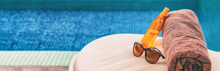 Suntan summer vacation panoramic of swimming pool background. Luxury banner background of sunscreen, sunglasses for sun protection on towel and lounger at hotel for sun tan relaxation.の写真素材