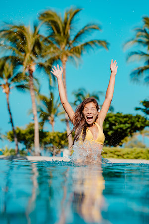 Travel resort concept. Happy fun woman jumping in pool screaming of joy at luxury hotel vacation. Multiethnic girlの写真素材