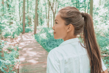Sustainable eco-friendly lifestyle happy Asian woman hiking on walking path in green forest during summer, young adult looking up at trees. Environment conceptの写真素材