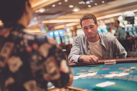 Casino gambling young man playing blackjack at table with cards and chips. Indoor portrait of gambler with dealerの写真素材