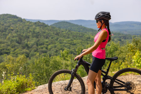 Woman on electric mountain bike in pink top, helmet and sunglasses, enjoying scenic forest view. eMTB conceptの写真素材