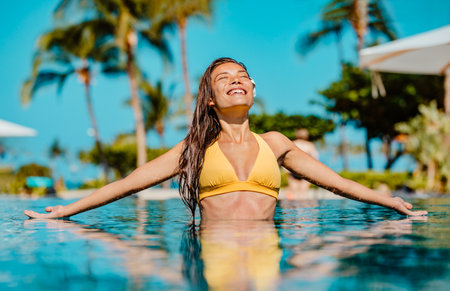 Summer sunbathing happy bikini woman swimming in infinity pool of luxury resort hotel relaxing on idyllic tropical travel vacation. Suntan solar skin care.の写真素材
