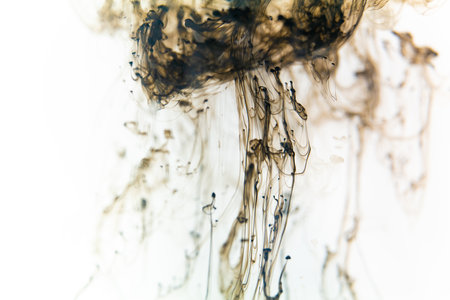 Black ink swirls forming delicate patterns as they diffuse elegantly through clear water, resembling...