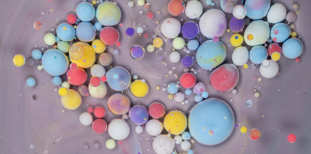 Colorful abstract art created by mixing paint and liquids on a gray surface, showcasing vibrant spheres in varying sizes and huesの写真素材