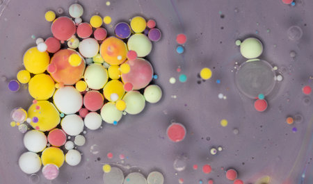 Colorful spheres blend and interact in a vibrant micro-world captured in close-up view on a neutral...