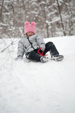 A girl in a snowy forest rides an ice slide down a slide. Photo of a child in a winter forest....