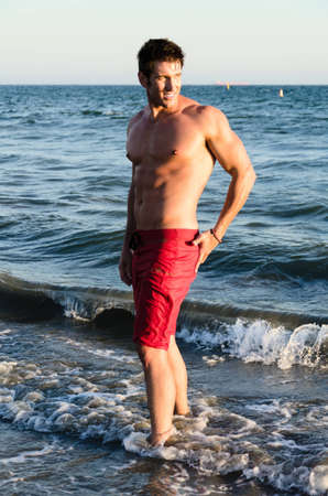 Gorgeous male model standing in the surf at the beach の写真素材