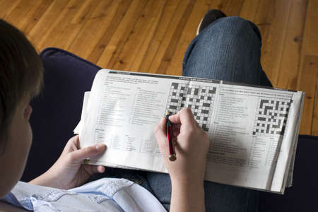A lady sitting on a sofa doing the crossword casually on her knee.の写真素材