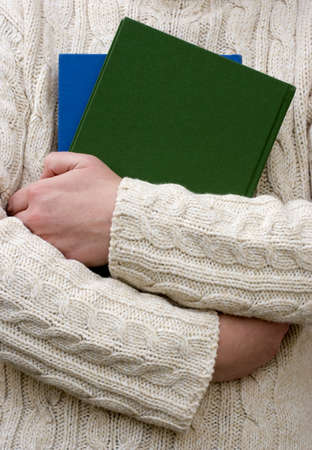 Person in a cosy woolen jumper carrying two colourful books.の写真素材