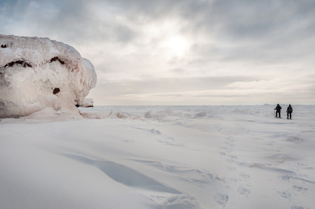 A man and women walks with snowshoes on the ice near the cliffsの写真素材