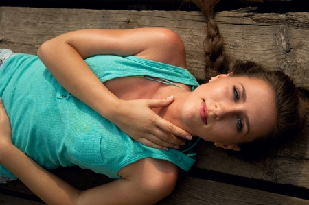 Pretty girl with tender makeup and manicured nails and a braid lying on wooden planks outdoorsの写真素材