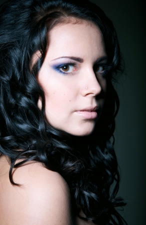 Studio portrait three quarters on black background of pretty brunette girl with shoulders, long shiny healthy curly hair, elegant blue makeup, mouth slightly open, looking at cameraの写真素材