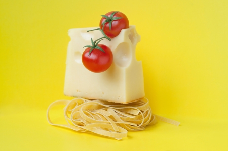 Colorful bright still life made of traditional Italian pasta nest, cheese with holes arranged above, two ripe fresh shiny red cherry tomatoes with green stems on top. Against yellow background, copy spaceの写真素材