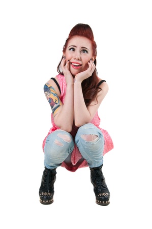 Pretty young rock woman model with cute red haircut, wearing pink spotted dress, ripped blue jeans, black boots with high heels and spikes, squatting, making faces and playing the apes, looking at camera  Isolated on whiteの写真素材