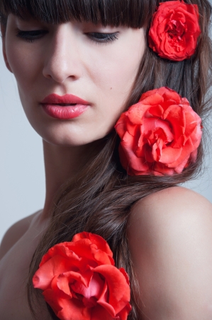 beautiful sensual young woman model with red lips, elegant long brunette hair weaved into waves with big fresh terracotta rosesの写真素材