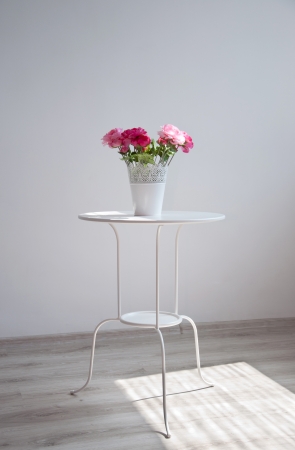 Pot with colorful red and pink rose flowers standing on a white tableの写真素材