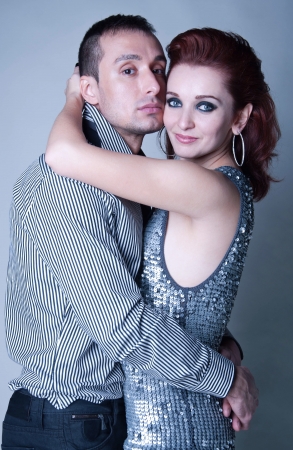 Tender young couple man and woman wearing elegant clothes cocktail dress, shirt, trousers, embracing each other, feeling love, passion, holding, hugging, looking at camera. Gray backgroundの写真素材