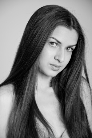 Black and white studio portrait of pretty young woman model with long healthy disheveled hair, looking at camera, smiling with mysterious smile, one eyebrow upの写真素材