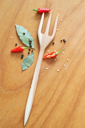 Kitchen still life made of wooden fork, red chili peppers cut and in whole, black pepper, bay leaves with wooden spoon on the wooden texture table background. Top viewの写真素材