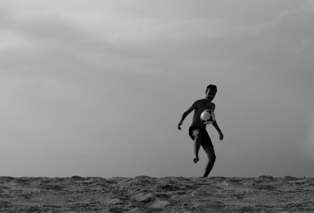 Black and white silhouette photograph of a young man playing soccer, kicking the ball on the sandy beach  Copy space の写真素材