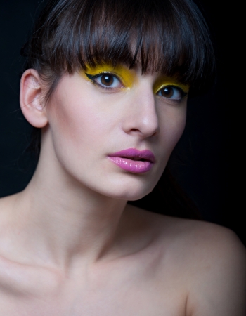 Studio portrait of young pretty woman model with bright yellow makeup, wearing pink lipstick, hair pulled back, looking at camera  Black backgroundの写真素材